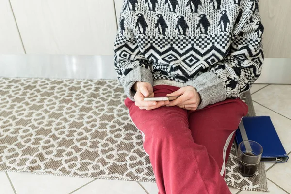 Woman using phone in home interior sitting on floor with tablet and coffee glass. Body part only. — Stock Photo, Image
