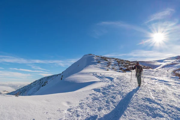 Backpacker kobiety trekking na śniegu w Alpach. Widok z tyłu, lifestyle zima, zimno uczucie, sun star w podświetlenie. — Zdjęcie stockowe