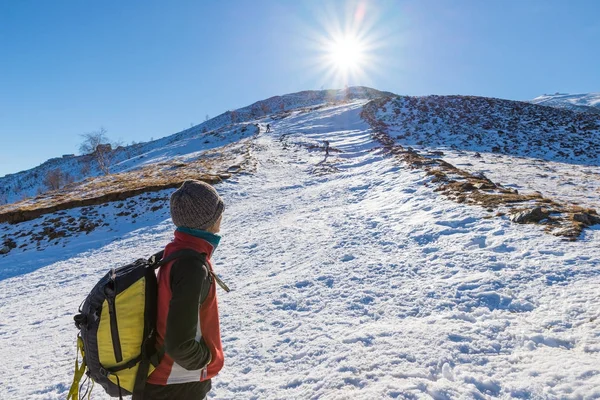 Vrouw backpacker trekking in de sneeuw op de Alpen. Achteraanzicht, winter levensstijl, koud gevoel, zon ster in tegenlicht. — Stockfoto