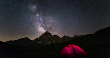 Samanyolu zaman atlamalı ve yıldızlı gökyüzünün Alpler (M. Viso, 3841 m, Piedmont, İtalya) yaz aylarında döner. Ön planda ışıklı kamp çadırı.