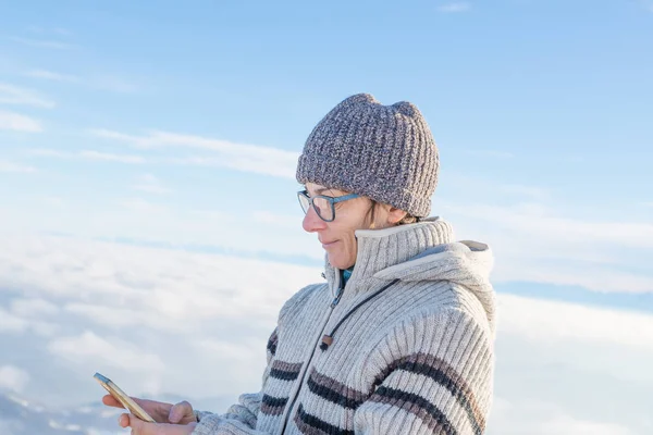 Uma mulher a usar um telefone inteligente nas montanhas. Vista panorâmica dos Alpes cobertos de neve na estação fria de inverno. Conceito de compartilhar momentos de vida usando novas tecnologias . — Fotografia de Stock