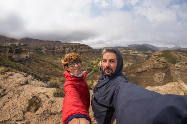 夫妇自拍与伸出的胳膊, 风山山顶, 金门高地国家公园, 南非。冒险和旅行的人的概念。鱼眼景观. — 图库照片