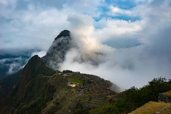 Machu Picchu iluminado por la luz del sol que sale de las nubes de apertura. La ciudad del Inca es el destino turístico más visitado en Perú. Niebla, nubes y niebla que cubren el valle . — Foto de Stock