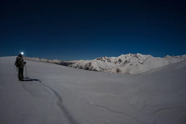 Snow on the Alps illuminated by moonlight, fisheye lens. Long exposure blurred two hikers looking at view, night outdoor activities.