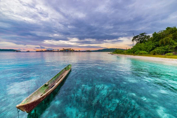 Tropisch strand, de Caribische zee, kano drijvend op transparant turkoois water, afgelegen Togean eilanden (Togian eilanden), Sulawesi, Indonesia. Dramatische hemel bij zonsondergang. — Stockfoto