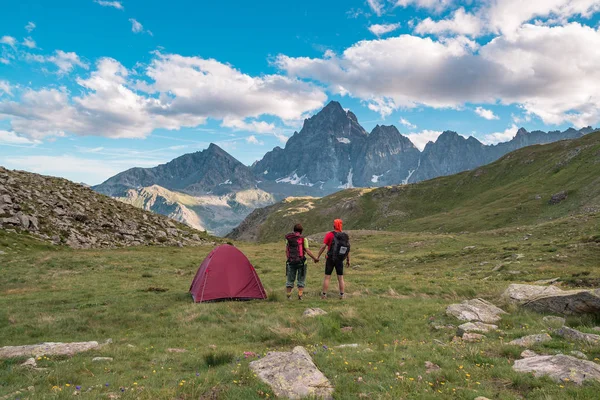 夫妇在阿尔卑斯山在日落时分的高处看发光的山峰的壮观景色。后视与野营帐篷，重点在背景中，色调和过滤图像. — 图库照片
