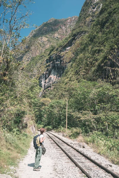 Mochilero caminando en la vía férrea a Machu Picchu, Perú, alternativa a la conexión de tren turístico habitual. Machu Picchu sitio arqueológico principal destino de viaje. Imagen tonificada . — Foto de Stock