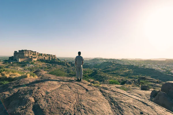 Turista de pie en la roca y mirando a la amplia vista de la fortaleza de Jodhpur desde arriba, encaramado en la parte superior que domina la ciudad azul. Destino de viaje en Rajastán, India . — Foto de Stock