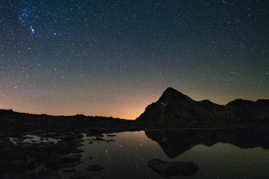 Astro yıldızlı gökyüzü göl Alpler üzerinde yüksek irtifada yansıyan. Orion takımyıldızı yönünde bulunan parlak.