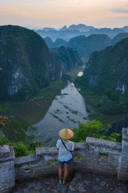 Tam Coc Vadisi, Ninh Binh Bölgesi, Unesco Dünya Mirası Alanı 'na bakan geleneksel Vietnam şapkalı kadın, Vietnam' da karst dağlarında sürünen manzaralı nehir..