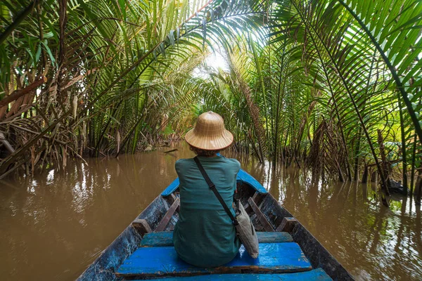 Prohlídka lodí v oblasti delty řeky Mekong, Ben Tre, Jižní Vietnam. Turista s vietnamským kloboukem na plavbě po vodních kanálech přes plantáž kokosových palem. — Stock fotografie