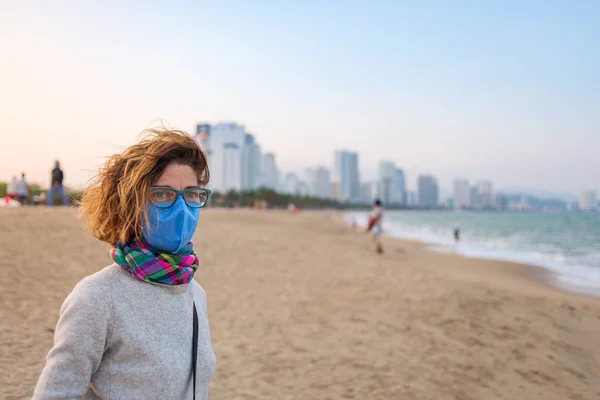 Белая женщина в санитарной маске на открытом воздухе на пляже Нячанг, знаменитая задержанная во Вьетнаме. Турист с медицинской маской защиты от риска китайской эпидемии пневмонии в Азии — стоковое фото