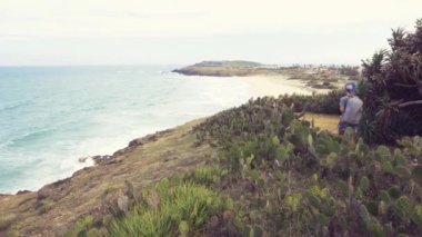 Ağır çekimde, sırt çantalı bir kadın tropikal sahilde uçurumda yürüyüş yapıyor. Vietnam 'a seyahat, Da Nang ve Nha Trang arasındaki Phu Yen bölgesi. Bai Xep muhteşem altın kumsal mavisi