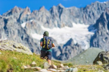 Sırt çantalı bir kadın dağın tepesine doğru yürüyor, manzaralı buzullar ve dramatik manzaralar yaz sporları seçici dikiz manzarası, özgürlük konsepti.