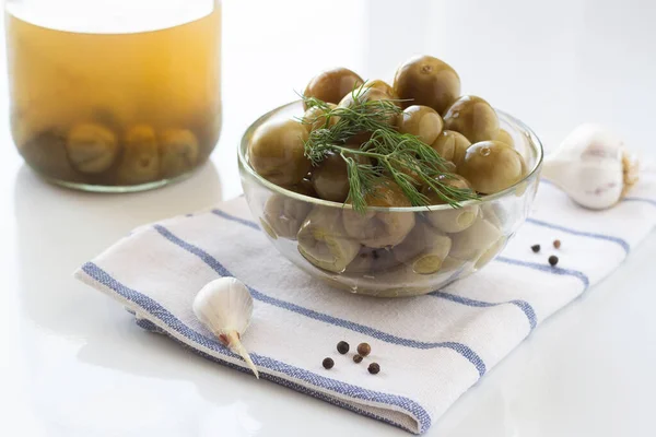 Beyaz arka planda beyaz bir havluyla cam bir tabakta dereotlu yeşil kiraz domatesleri.