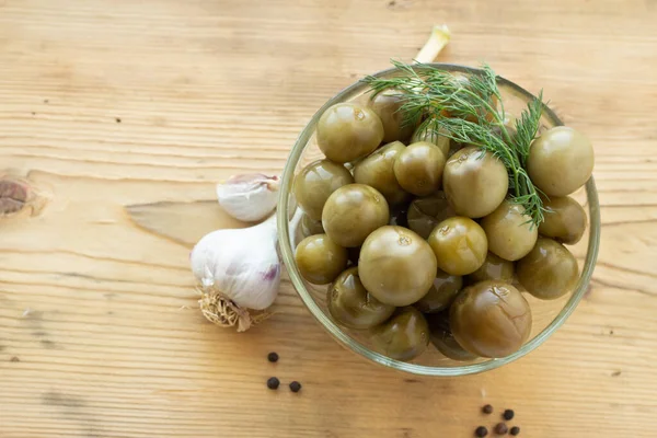 Sour green cherry tomatoes with dill in a glass plate on a wooden background with garlic and black pepper — ストック写真