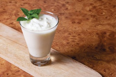 Cam bir kadehte Kefir, üzerinde nane şekeri dalı olan kahverengi bir arka planda tahta tahta bir tahta.