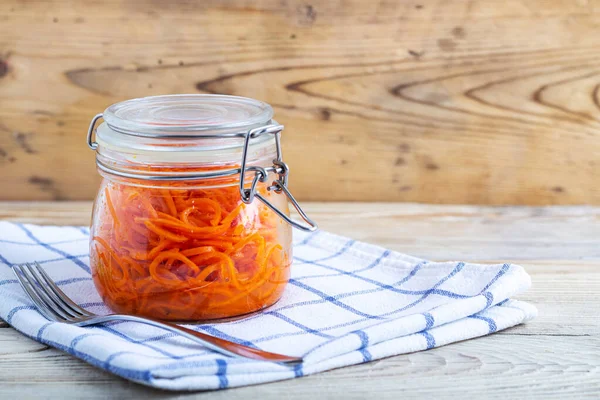 Korean carrots in glass jars on a white towel on a wooden table
