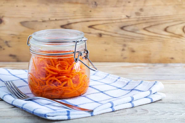 Cenouras coreanas em jarros de vidro em uma toalha branca em uma mesa de madeira Imagem De Stock