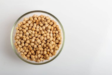 Beyaz arka planda yuvarlak cam bir tabakta kurumuş nohut.