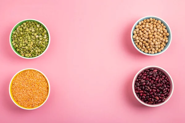 Frijoles secos, lentejas, cuerno verde y garbanzos en platos redondos sobre fondo rosa —  Fotos de Stock