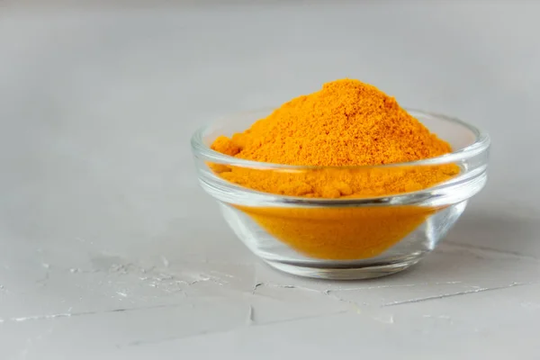Ground turmeric in a glass plate on a gray background — Stock Photo, Image