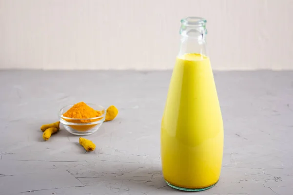 Gri arka planda, cam bir şişedeki altın süt