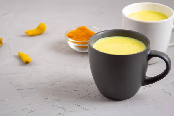 Gri arka planda iki bardak altın süt.