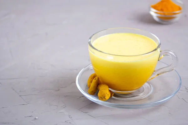 Goldene Milch in einer gläsernen grauen Tasse auf grauem Hintergrund — Stockfoto