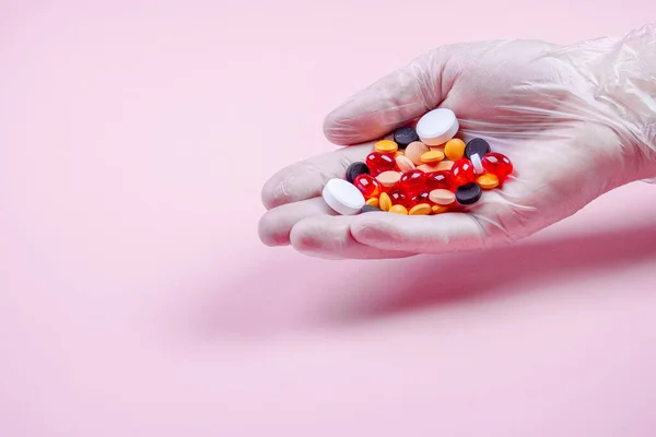Manos de hombre en guantes de goma blanca sostienen muchas píldoras multicolores sobre un fondo rosa —  Fotos de Stock