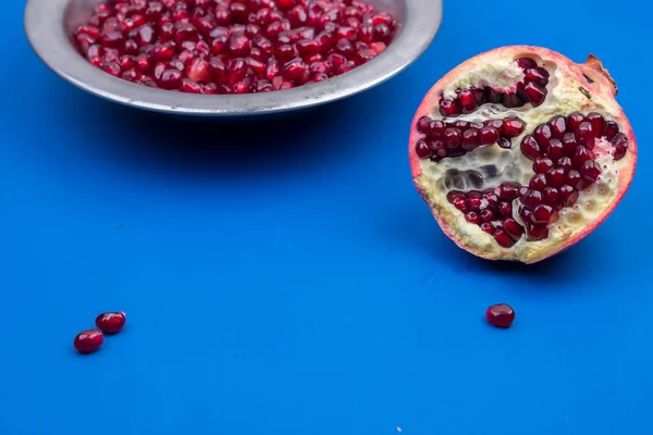 Pomegranate grains in a metal plate and half ripe pomegranate on a blue background — Stock Photo, Image