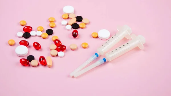 Dos jeringas médicas y píldoras multicolores yacen sobre un fondo rosa —  Fotos de Stock