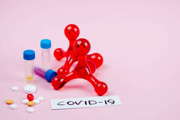 Tek kullanımlık tıbbi maske ve beyaz haplarla dolu su toplayıcı pembe arka planda yatıyor.