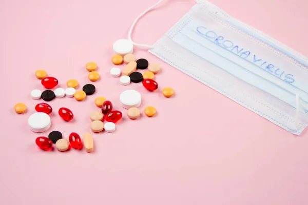 Máscara médica desechable y ampolla con píldoras blancas se encuentran sobre un fondo rosa —  Fotos de Stock