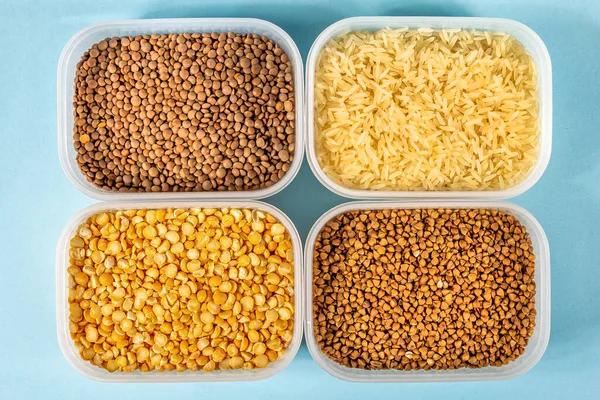 Çiğ pirinç, karabuğday ve kuru bezelye mavi arka planda plastik kaplarda.
