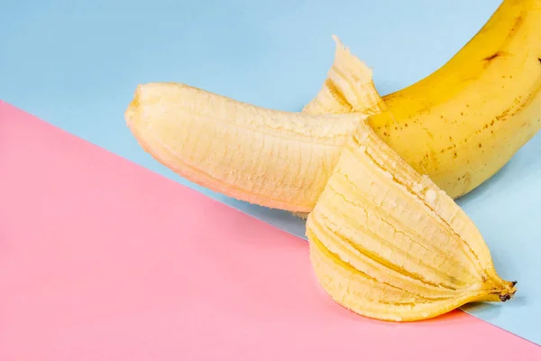 Ugly yellow banana with black spots on a pink and blue background close-up