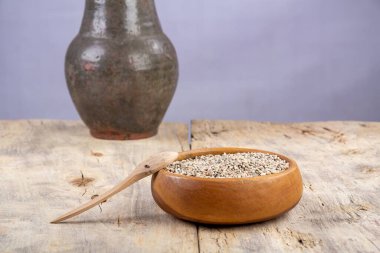 Ahşap bir masada, ahşap bir tabakta soyulmamış çiğ yulaf. Arka planda kilden bir sürahi var. Ülke biçimi