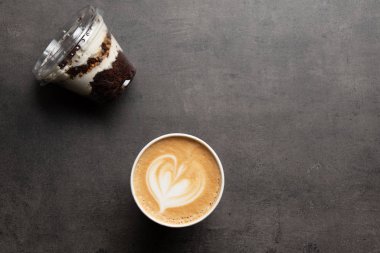 Plastik kapta tatlı ve gri arka planda bir fincan kapuçino.