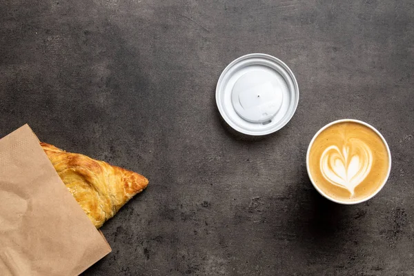 Samsa kağıt zarfta, cappuccino kağıt bardakta ve gri arka plan görünümünde.