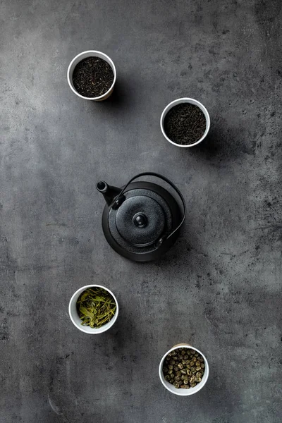黒ティーポットと濃い灰色の背景に紙コップで4種類のお茶 ロイヤリティフリーのストック画像