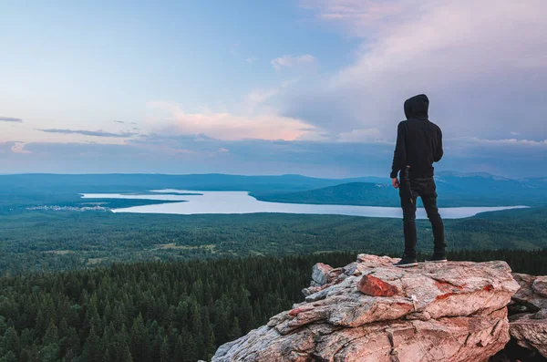 バレーと湖を見てZyuratkul国立公園の山の頂上に岩の上に立っている孤独な男 ストックフォト