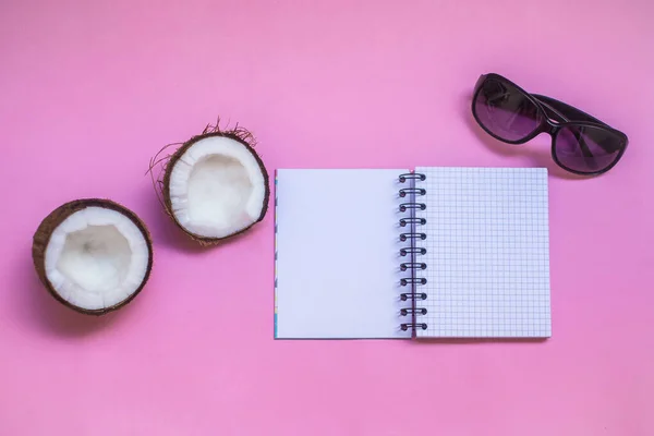 Vacation and travel concept. Traveling kit. Note book with summer shoes, sunglasses, exotic fruit coconut on the pink background.