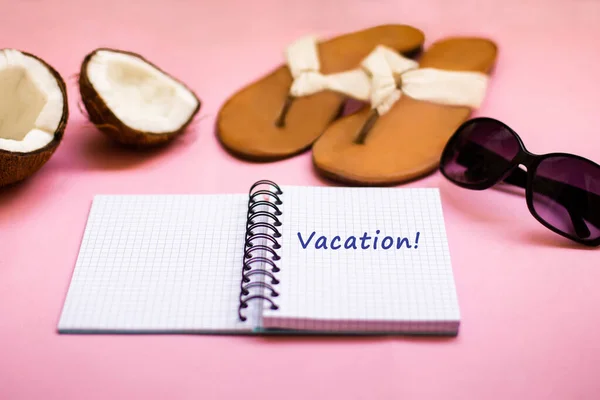 Vacation and travel concept. Traveling kit. Note book with summer shoes, sunglasses, exotic fruit coconut on the pink background.