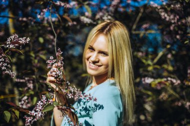 Çiçek açan ağaçtaki güzel bahar kızı. Bahar geliyor. Baharda çiçek açmış bahçede genç bir kadının portresi. Mavi elbise..