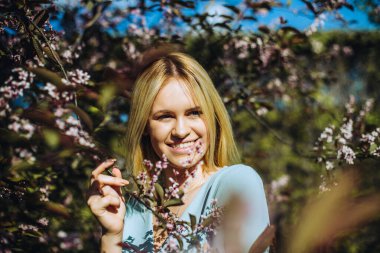Çiçek açan ağaçtaki güzel bahar kızı. Bahar geliyor. Baharda çiçek açmış bahçede genç bir kadının portresi. Mavi elbise..