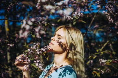 Çiçek açan ağaçtaki güzel bahar kızı. Bahar geliyor. Baharda çiçek açmış bahçede genç bir kadının portresi. Mavi elbise..