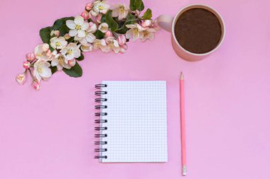 Notlar için bir defter pembe arka planda duruyor, kalem, kahve ve çiçeklerin yanında. Kişisel zaman ve iş planlama   