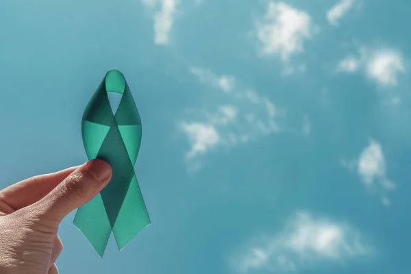 Hand holding Teal Ribbon over blue sky, Ovarian Cancer, cervical