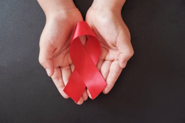 Kırmızı arka planda kırmızı kurdele tutan eller, HIV farkındalığı.