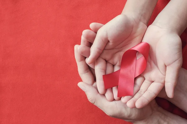 Manos sosteniendo cinta roja sobre fondo rojo, conciencia de VIH cóncavo —  Fotos de Stock